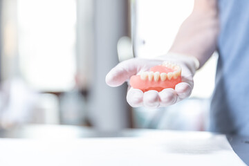 Artificial upper teeth on gloved hand in modern dental office  
