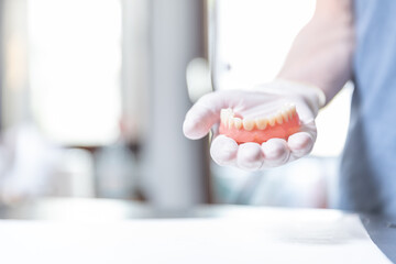Upper denture resting on gloved hand in bright dental clinic    © SWMedia