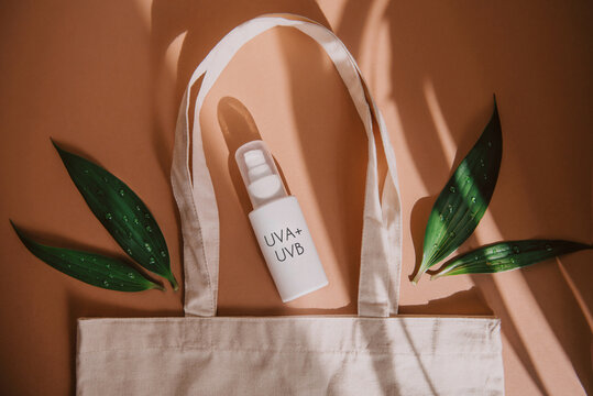 top view of eco bag with cosmetic product SPF cream and green leaves on orange background