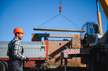 A builder controls a crane while unloading panels to cover a house