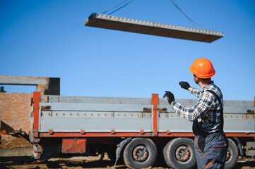 The builder controls the unloading of the panels for the roof of the house with a crane