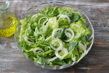 Fresh green salad with onion rings and dressing on rustic wooden table, healthy organic meal top view