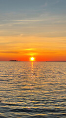 Beautiful sunset over the sea. The sun sets on the water. The sky is painted with bright colors. Sunny path on the water. Summer evening. Sunset beach. Vertical photography.