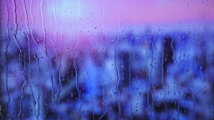 Rain drops on window with purple and blue city lights