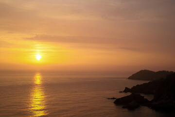Spectacular Sunset Over Calm Waters: A Breathtaking View of the Sun Setting on the Horizon at Dusk Behind Serene Ocean Waves and Rocky Shorelines