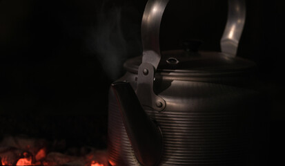Atmospheric kettle in camping boiled on a fire on coals at night in nature