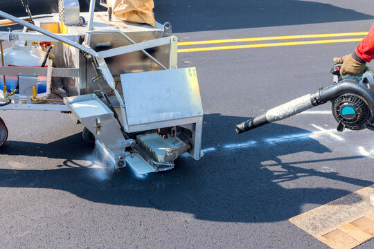 Workers operate road striping machine on newly paved street while ensuring accurate paint application for safety.