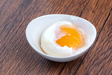 A soft-boiled egg in a white bowl on a wooden table.