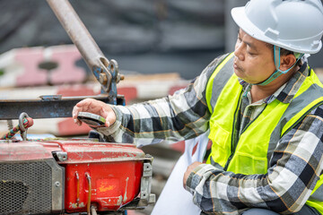 Construction worker wea safety helmet and reflective vest checking machinery at a building site du...