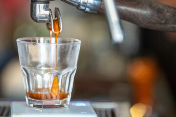 Close-up of a rich dark coffee being poured from a vintage metallic espresso machine spout into a...