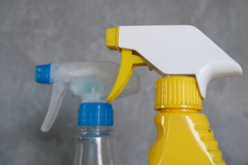 Two plastic spray bottles, one yellow and one clear, positioned against a neutral gray background,...