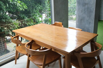 Sleek wooden dining table with matching chairs placed near large windows, letting in natural light and green outdoor views.