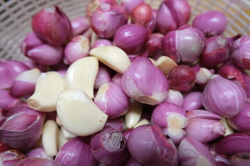 Freshly peeled garlic cloves and shallots in a basket, essential aromatic ingredients used widely in Indonesian culinary dishes.
