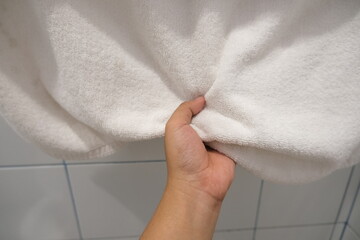 Hand gripping soft white towel in bathroom
