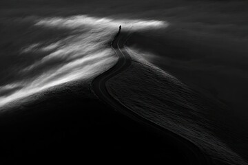 A winding road, seemingly lost in a sea of mist, leads into a dark, ethereal landscape. A solitary figure traverses the road