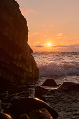 Captivating sunset over rugged coastline, featuring crashing waves and a warm, golden sky. Scene evokes calmness and serenity, embracing nature's raw beauty