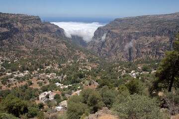 High-angle view of a valley, village, and mountains.  A low cloud layer fills a deep ravine