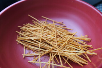 Close-up of crispy Indonesian mie lidi snack sticks, served in a pink bowl. A popular spicy and crunchy street food treat.
