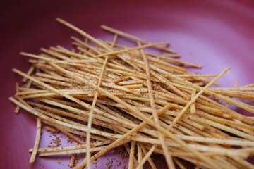 Close-up of crispy Indonesian mie lidi snack sticks, served in a pink bowl. A popular spicy and crunchy street food treat.
