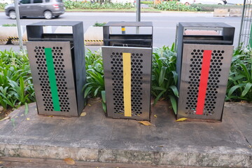 Set of three metal trash bins with green, yellow, and red markings placed on a sidewalk for waste...