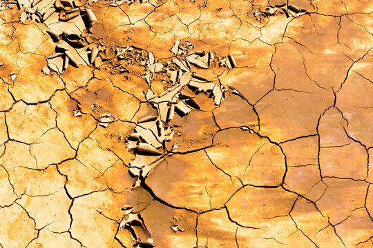Detail shot of mottled orange and yellow mud and clay that is cracked and peeling