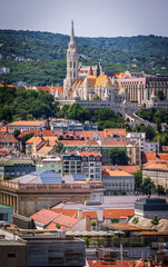 Panoramic view of Matthias Church and Fisherman's Bastion in Budapest, with Buda Hills in the background, captured from the dome of St. Stephen’s Basilica on a sunny summer day.