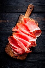 Sliced cured ham is artfully arranged on a wooden cutting board, showcasing its rich color and texture, ideal for serving at gatherings or enjoying as a snack