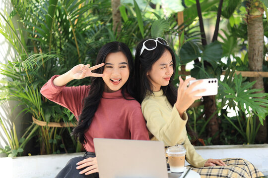 Asian Woman Friends Using Smartphone Selfie Together while Sitting at Outdoor Coffee Shop