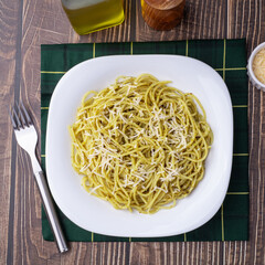 Italian pasta spaghetti on a plate with pesto sauce and parmesan cheese