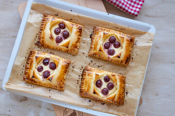 Fresh and homemade baked puff pastry pockets with quark cherry filling on a baking tray