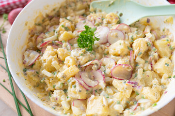 Healthy potato salad with yoghurt dressing, chives, red redish, onions and pickles in a bowl