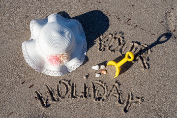 Holiday sign and toys on sandy beach with sun hat