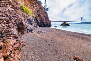 Kirby Cove Beach in California with red sand, blue ocean waves, and dramatic cliffs covered in pine...