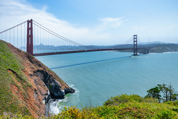 Iconic view of the Golden Gate Bridge stretching across the blue waters of the San Francisco Bay, seen from a green cliffside near Kirby Cove. A timeless symbol of California travel and nature