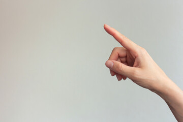 Close-up photo of a woman's index finger pointing at an empty gray background, ordering something...