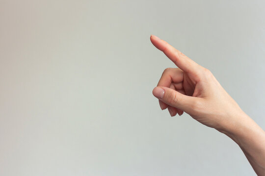 Close-up photo of a woman's index finger pointing at an empty gray background, ordering something on a virtual screen