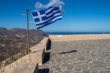 Greek flag waving on a viewpoint overlooking mountains and sea in crete, greece