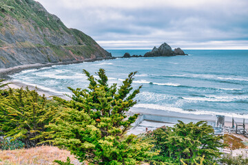 View of San Pedro Rock off the coast of Pacifica, California. Rugged cliffs and waves roll into a...