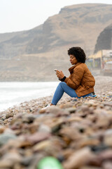 Woman using smartphone on rocky beach, changing routine, enjoying nature