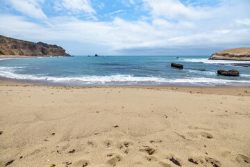 Golden sand and rocky shoreline at Greyhound Rock Beach on the California Pacific Coast. Scenic ocean view along Highway 1 with dramatic cliffs and turquoise waves under a partly cloudy sky