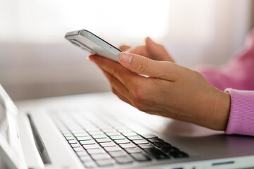 Close-up of hands holding a smartphone and typing on a laptop keyboard, depicting a blend of...