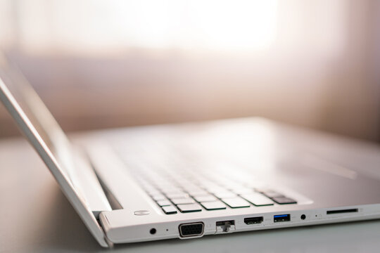 A close-up side view of a modern silver laptop, highlighting its keyboard and various ports with a soft, blurred background.