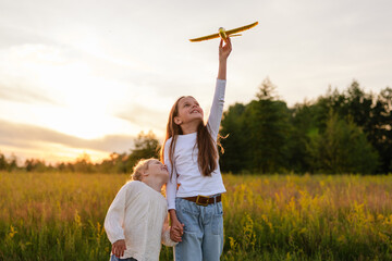 
Two young girls in a golden field, one holding a toy airplane high, look up at it with wonder...