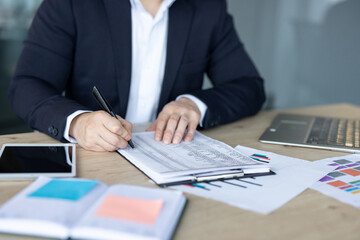 Close-up photo of the hands of a young man in a suit sitting at his workplace in the office, working with documents, writing papers by hand