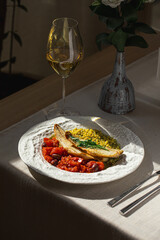 Portion of coooked sea bass fillet with ptitim tomatoes and olives with wine
