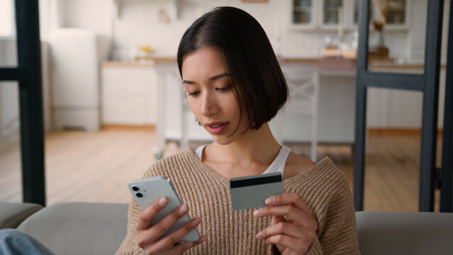 Hispanic woman female shopper buyer customer girl lady homeowner online shopping buying goods with mobile phone credit card payment internet store using bank app pay order food delivery kitchen home