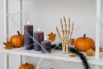 decorative halloween display featuring purple candles, a skeleton hand, and pumpkins amidst autumn leaves and spider webs for festive ambiance