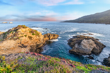 Scenic coastal view at Garrapata State Park near Big Sur, California, showcasing rugged cliffs, vibrant plants, and the Pacific Ocean along the iconic Highway 1 on a clear spring day