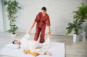 Masseuse making thai yoga massage. Woman therapist doing traditional massage treatment, stretching...