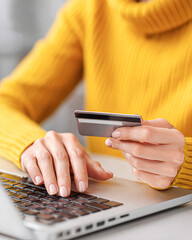 Person wearing a yellow sweater making an online payment using a credit card and laptop keyboard.
